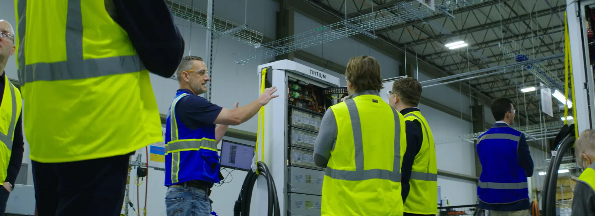 Tritium engineer walking visitors through an open charger cabinet on the Tennessee factory floor